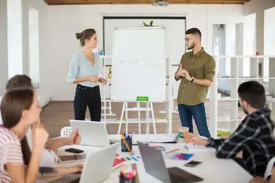 man-eyeglasses-shirt-smiling-woman-blouse-standing-near-board-while-dreamily-presenting-new-project-colleagues-group-young-people-working-together-modern-white-office