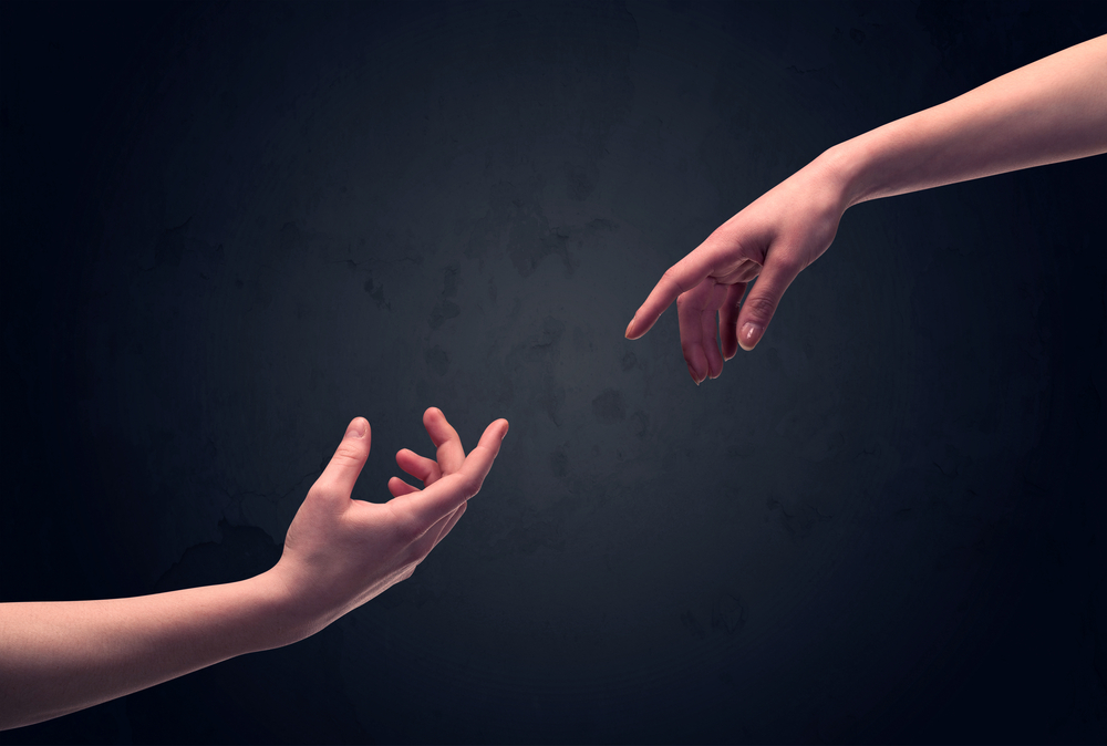 Two male hands reaching out to one another, almost touching, in front of dark clear empty background wall concept-1